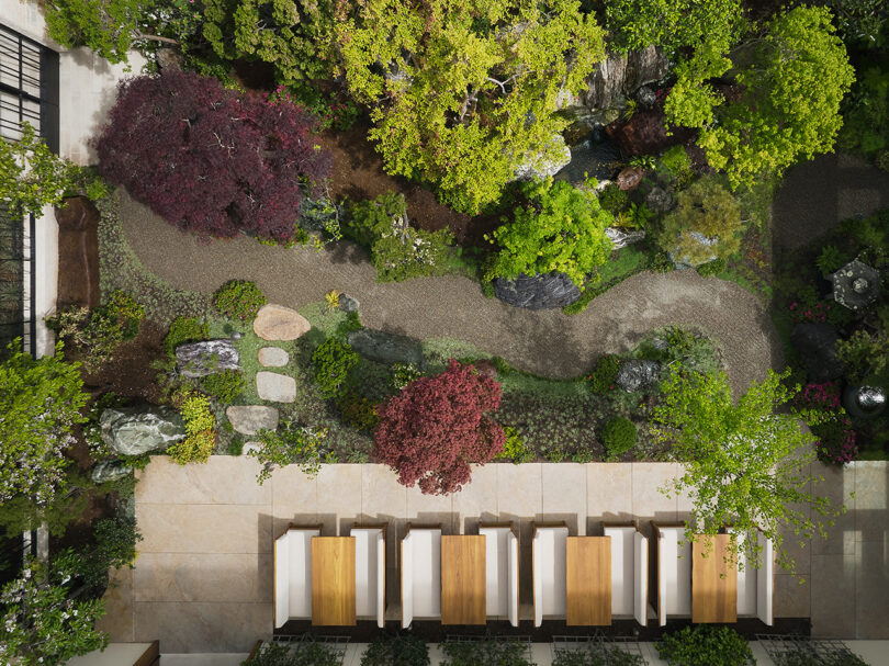 Overhead drone photo of gravel footpath winding through Nobu Hotel Palo Alto's restaurant Japanese style garden, showing various planting zones and rock placement, with four dining tables situated at the bottom.