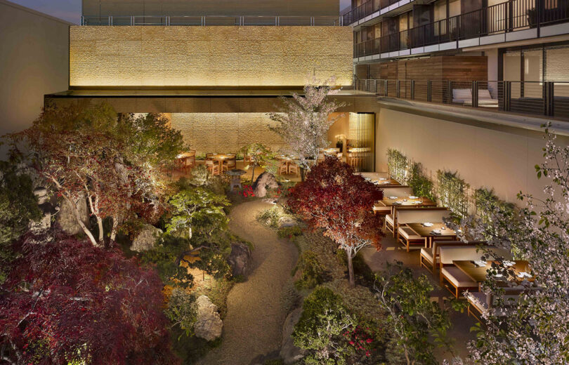 Overhead view of Japanese rock garden landscaped with California native plants illuminated at dusk with dining tables lined up along the right against hotel wall.