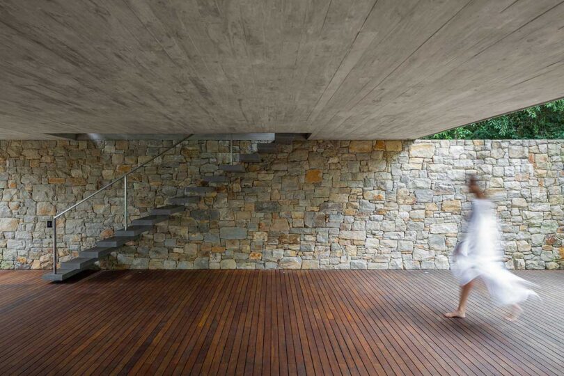 covered wooden deck with floating stairs rising by stone wall