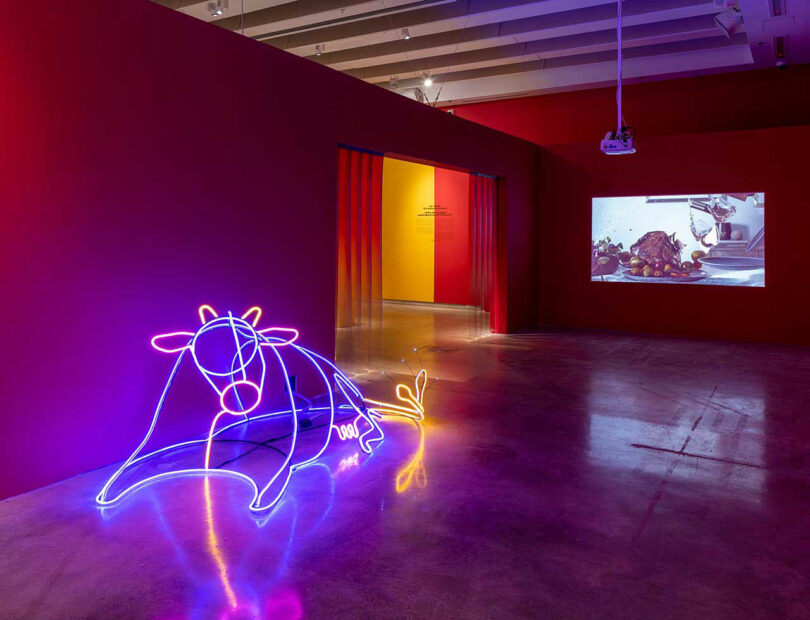 angled gallery room with neon three-dimensional bull with projector in background