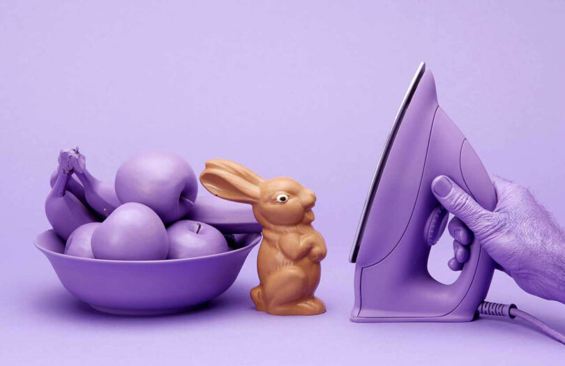 A chocolate bunny on a lavender backdrop with matching bowl of fruit and an iron