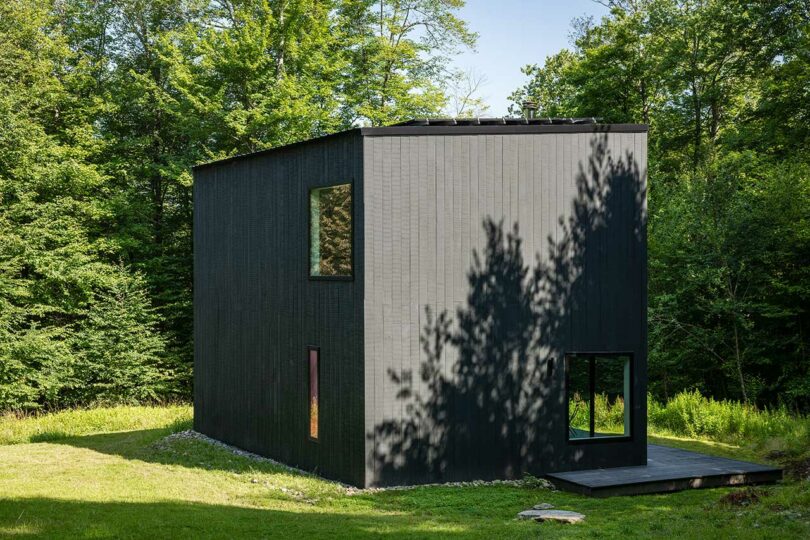 angled corner exterior view of modern black box house surrounded by trees