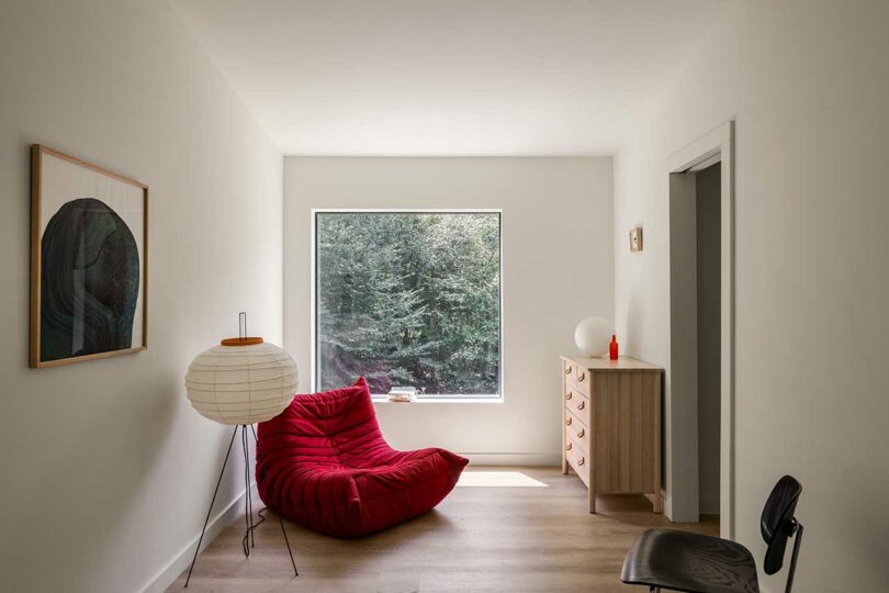 interior space with red Togo chair, lamp, and wooden dresser staged in front of square window