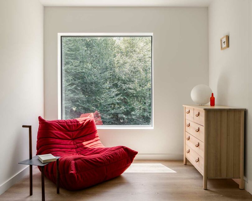 interior space with red Togo chair, lamp, and wooden dresser staged in front of square window