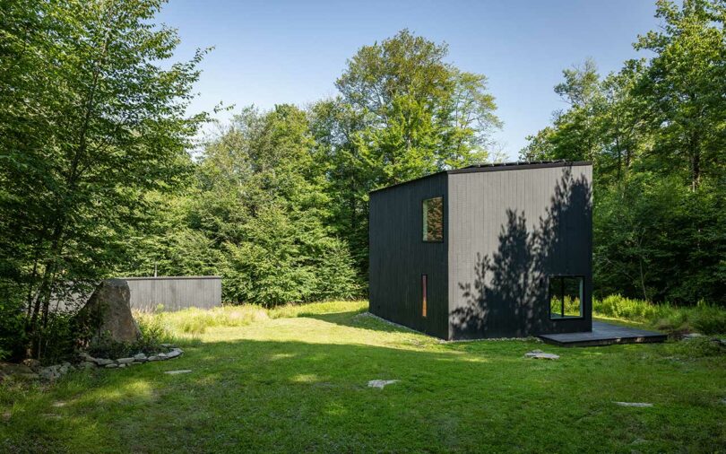 distance corner exterior view of modern black box house surrounded by trees