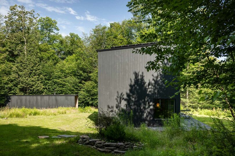 side view of modern black box house surrounded by trees