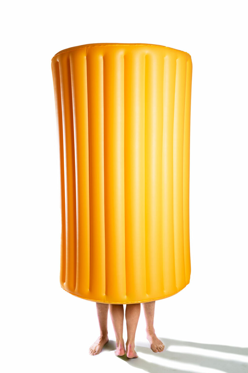 long yellow pasta shaped pool float tube with people legs sticking out from bottom
