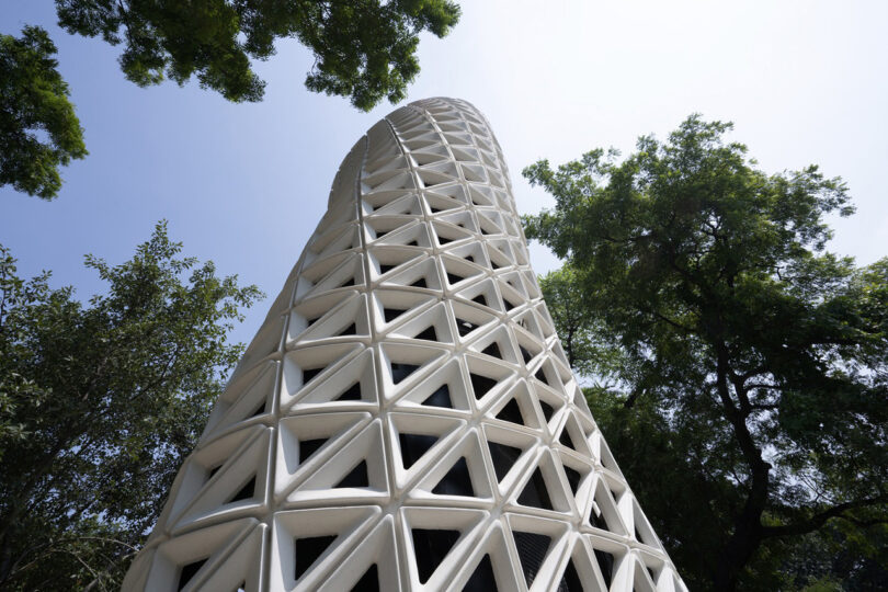 White lattice design VERTO air purifier tower surrounded by trees and blue skies above it.
