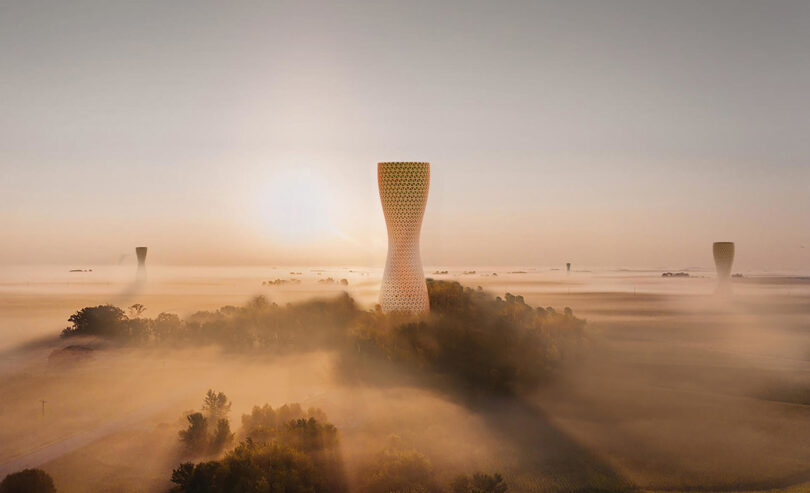 3D render of Studio Symbiosis Aũra Hive tower concept, a 60 meter tall air filtration tower rising above a foggy morning sky from a small group of trees with several other Aũra Hive towers visible in the distance.
