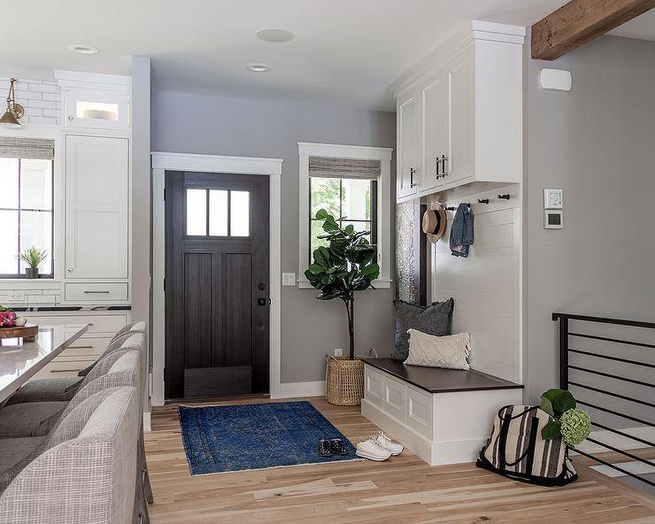 Entryway boasts a small mudroom that features a blue over-dyed rug at a dark brown Craftsman style door and a white and brown mudroom bench with built-in cabinets above.