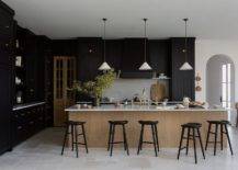 Kitchen features black cabinets and a brown island with brushed gold deck mount kitchen faucet with black tractor stools, lit by white and gold vintage lanterns.