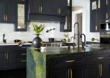 Contemporary kitchen features a green and black marble waterfall island with a matte black pull out kitchen faucet, and antiqued mirrored black cabinets with modern brass pulls topped with ivory and black marble.