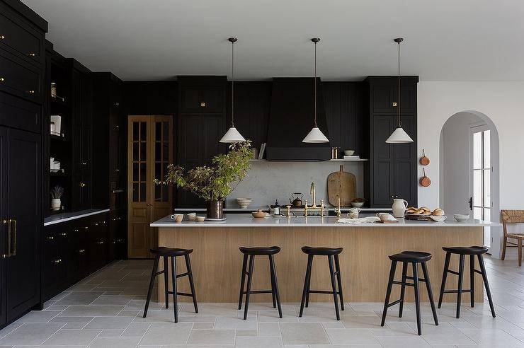 Kitchen features black cabinets and a brown island with brushed gold deck mount kitchen faucet with black tractor stools, lit by white and gold vintage lanterns.