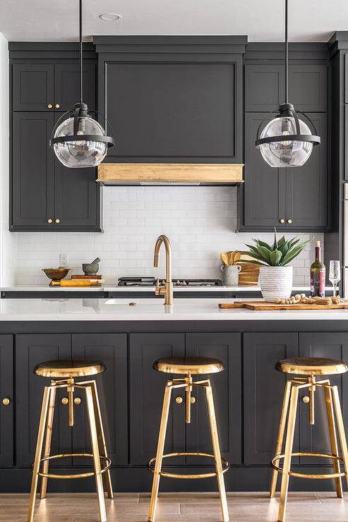 Black and white kitchen features brass swivel stools at a black island with gold gooseneck facuet.