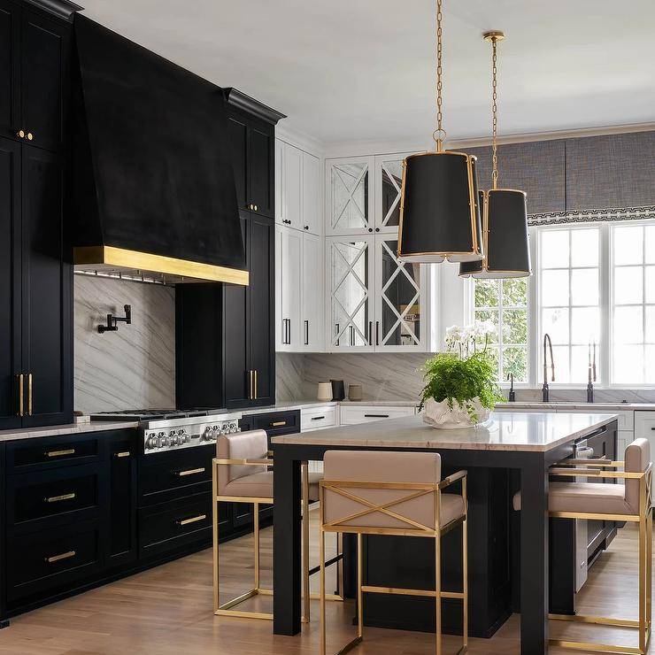 Gold and black hanging shade lights illuminate a marble island top accenting a black kitchen island seating gold and blush pink stools.