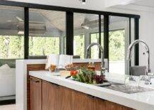 A brown veneer kitchen island is fitted with a wide stainless steel sink paired with two chrome gooseneck faucets