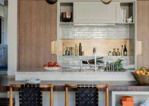 Wonderfully designed modern kitchen boasts wood and black woven leather stools placed at a wood top island finished with cookbook shelves.