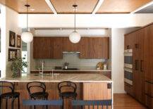 A clean mid-century kitchen with dark wood cabinets, black metal chairs, and an island with a sink.