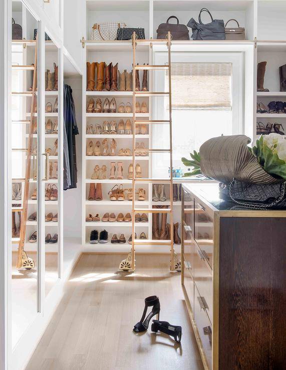 Walk-in closet boasting a ladder on rails styled with custom built-in shoe shelves and purse cubbies. This large yoastmark class=