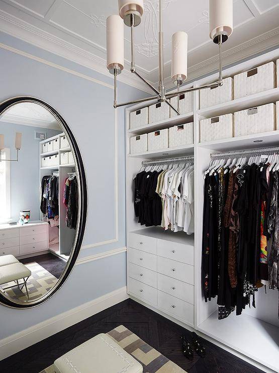 White and blue custom walk in closet features a full length oval mirror, white built in drawers and white woven baskets on upper shelves.