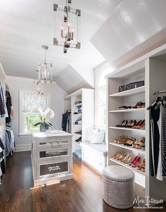 Sun-filled walk-in closet boasts a white closet island adorned with mirrored drawers and topped with marble. A built-in closet window seat is flanked by tall shoe shelves.