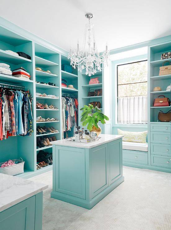 Turquoise blue walk-in closet features a window seat bench under a window surrounded by blue built-ins with glass knobs. This large yoastmark class=