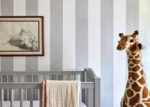 Boy's nursery features a gray crib on gray vertical stripe wallpaper and a tall stuffed giraffe.