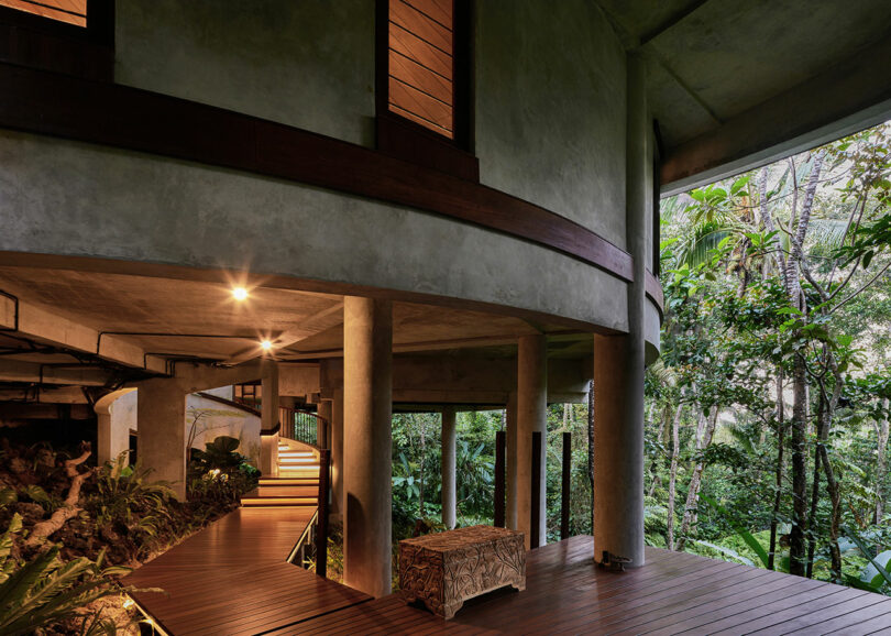 covered wooden walkway below concrete house surrounded by greenery