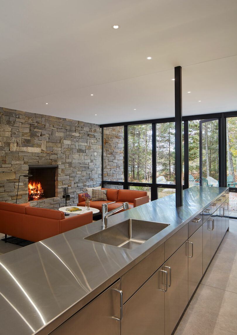 angled interior shot of modern living room with stone walls, industrial kitchen, and orange leather seating
