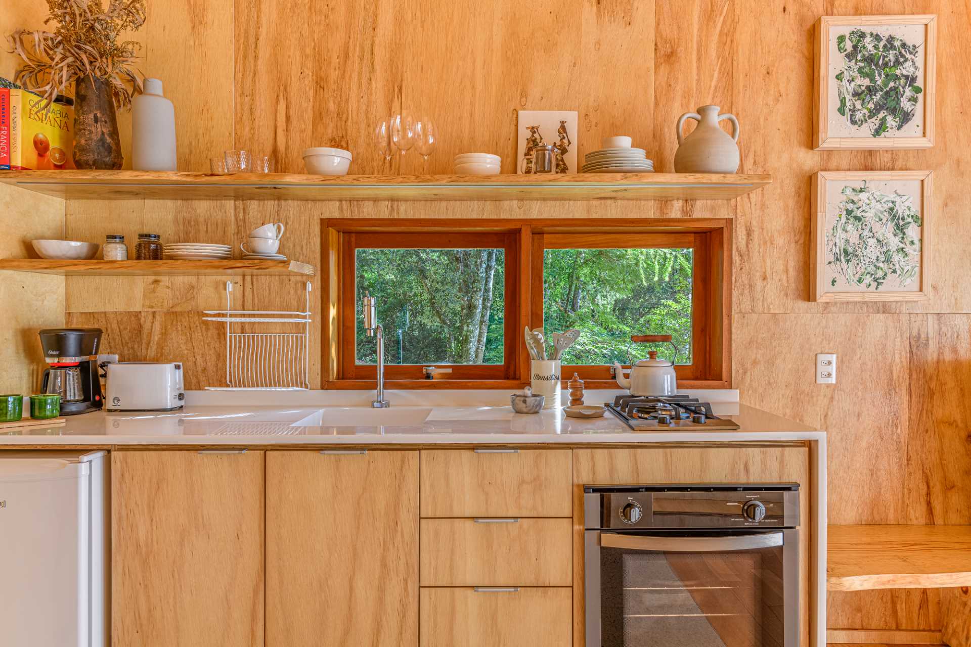 A modern tree house kitchen that includes wood cabinets, a white countertop, and floating shelves that provide additional storage.
