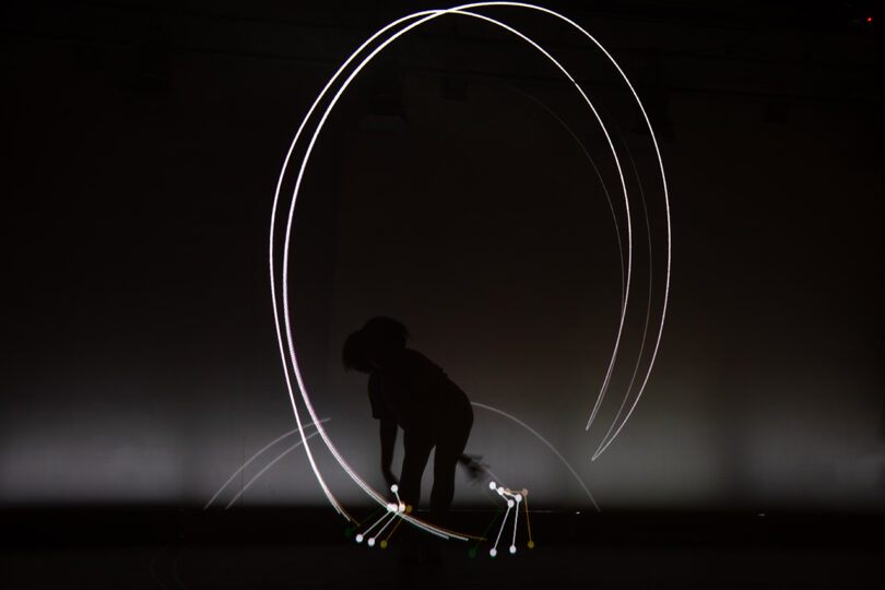 person dressed in black uses light to create tracers on a black background