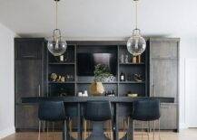 Black leather stools at a basement bar features gold base complimenting brass and clear globe pendant lights.