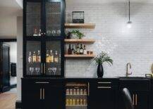 Basement wet bar with black lattice front cabinets features a glass front beverage fridge and oak floating shelves gray glazed offset tiles.