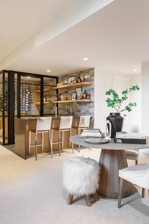 Basement bar features a round wood and concrete pedestal table accented with a white faux fur stool and white upholstered chairs.