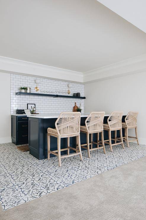 Candelabra Home Loom Barstools at a navy blue bar island designed ina basement wet bar finished with white subway tiles, gray grout and white quartz countertops. Ivory and blue mosaic floor tiles add a charming look to the basement