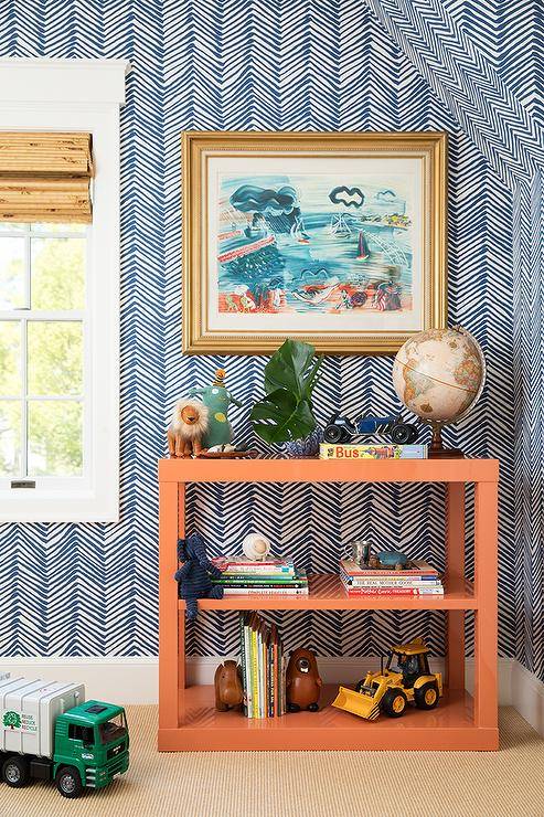 Wonderfully styled orange and blue boys' bedroom features an orange lacquer shelving unit placed beneath a gold-framed art piece hung from a wall finished with Quadrille Petite Zig Zag Wallpaper.