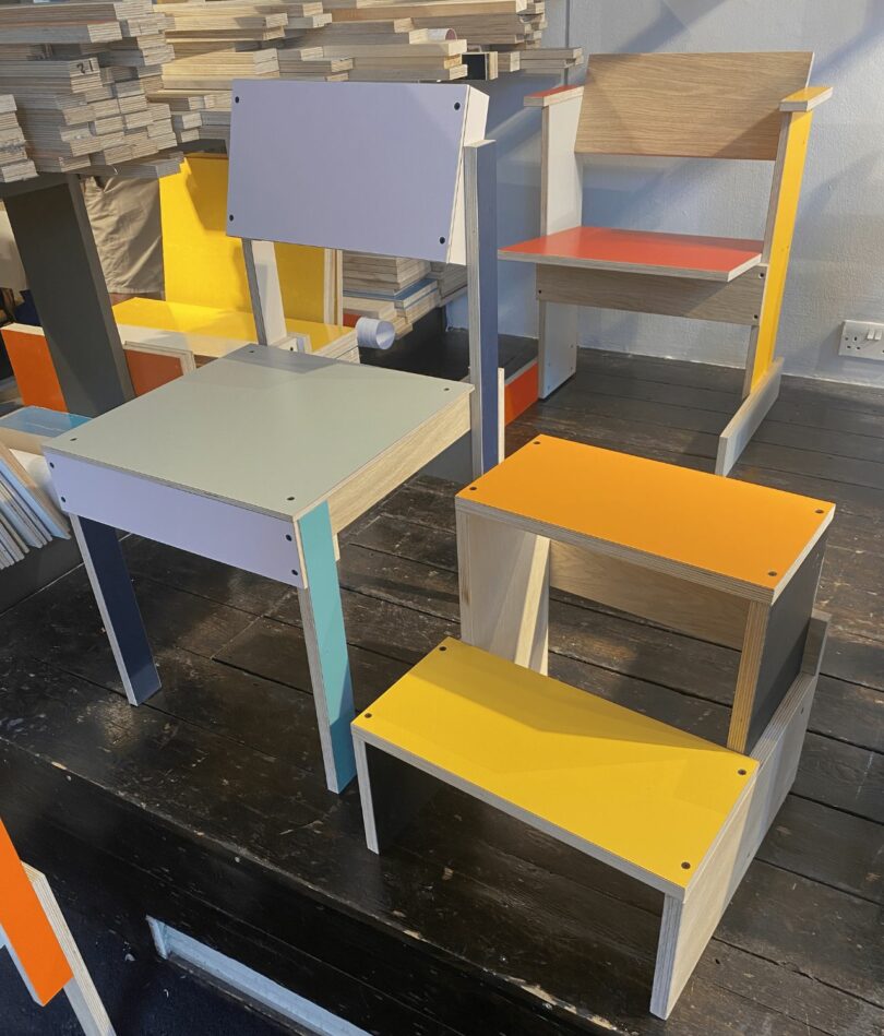 Two chairs and a set of steps are made from flat pieces of brightly colored plywood. 