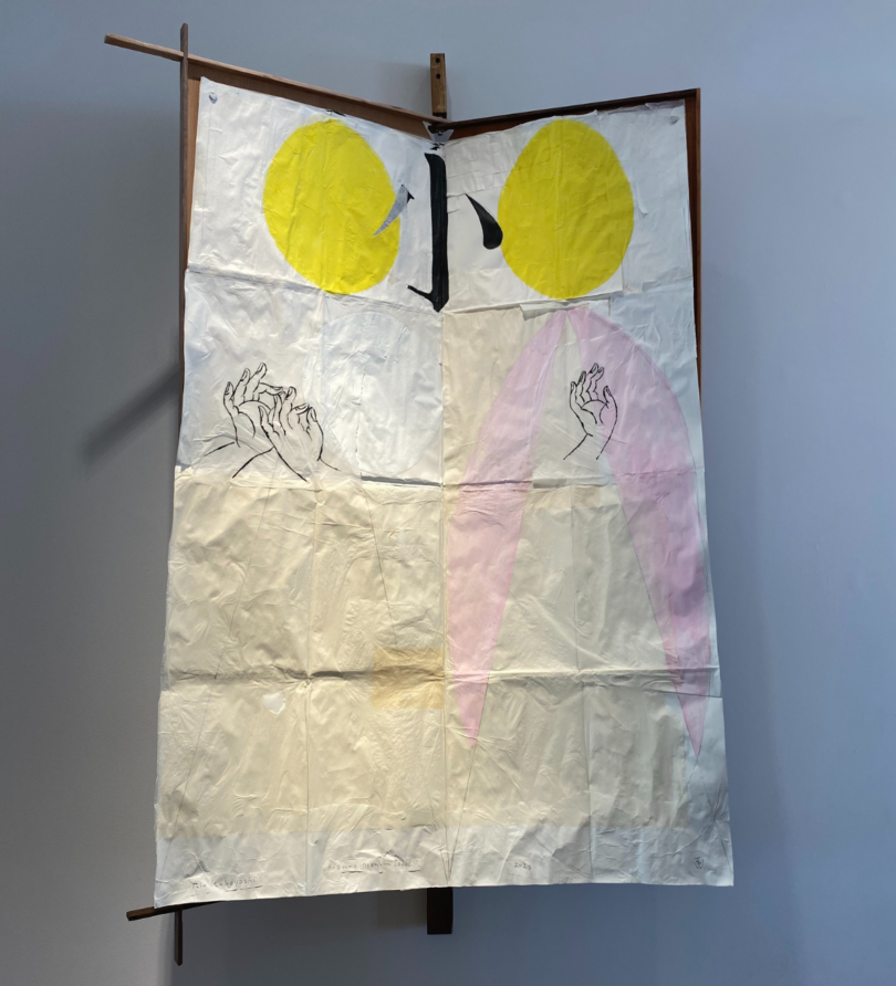 A poster featuring two yellow circles, a Japanese character in black and three illustrated hands has creases from having been folded and is hung from a wooden frame. 