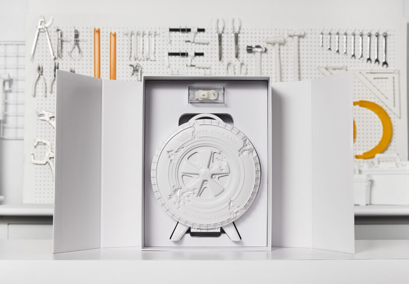 Packaging and display of the Eroded Super Rally Case shaped like car wheel and tire, with Daniel Arsham's Silkstone Porsche in a clear case above it in a slot in the box.