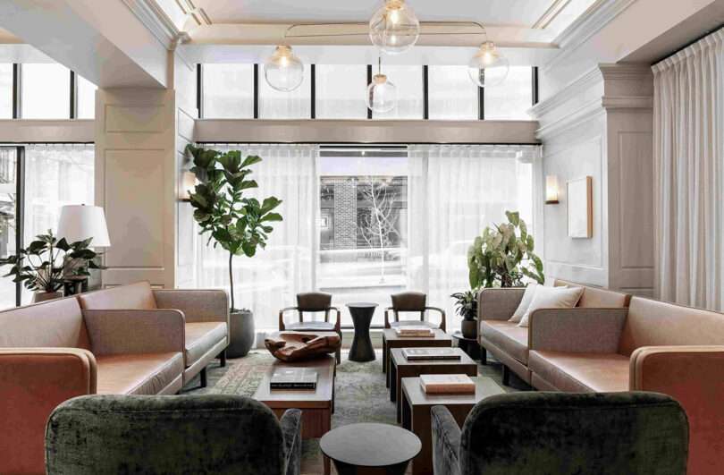 Hotel lobby with globe brass chandeliers overhead and four large leather sofas facing one another with armchairs in between, forming a rectangle. Large windows look out onto the streets of Downtown Portland.