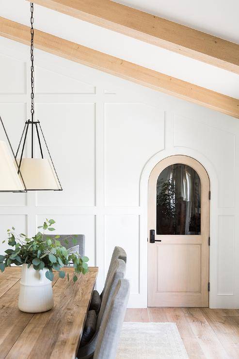 Cottage dining space designed with board and batten trim, an arched door and beams on a vaulted ceiling.