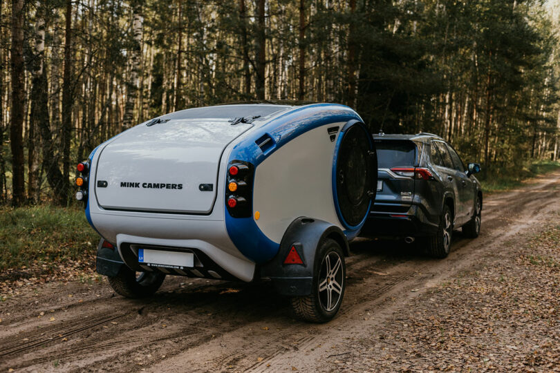 angled side view of gray and blue teardrop camper in woods