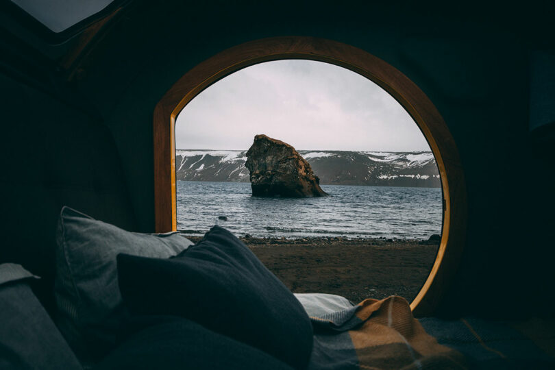 view from inside camper looking through round doorway at ocean with large rocks