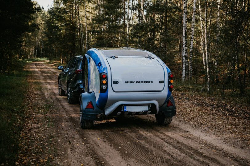 back view of gray and blue teardrop camper in woods