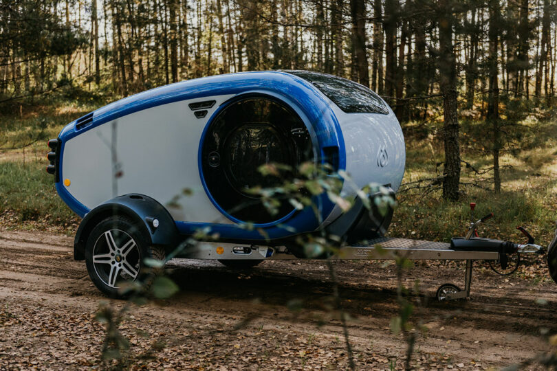angled side view of gray and blue teardrop camper in woods
