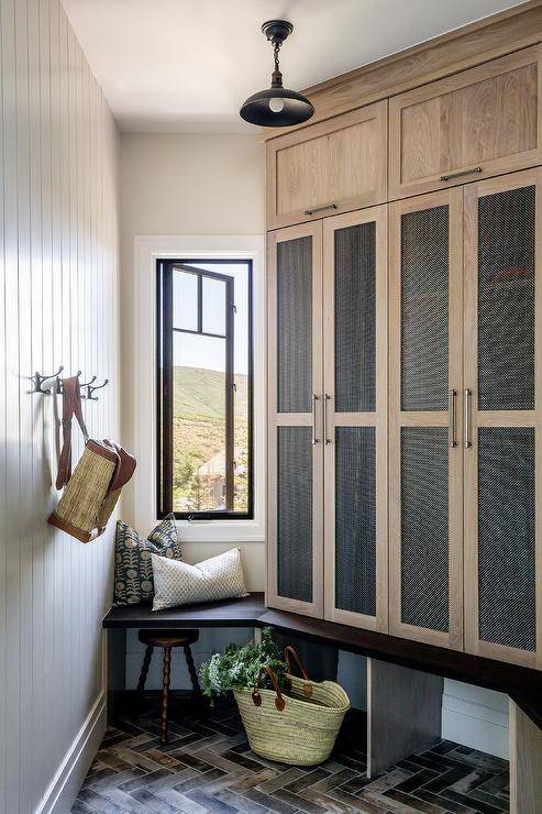 Cabin-styled angled mudroom features mesh lockers, a small built-in window bench, and herringbone floors.