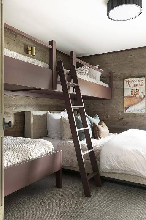 Country bedroom design features brown loft beds on oak plank walls with a brown loft bed ladder and a gray wingback bed under loft bed.