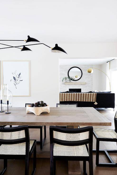 White and black cane dining chairs at a gray wash dining table in a transitional room with modern and Scandinavian aesthetic boasts a large black 6 arm chandelier for a stunning finish.