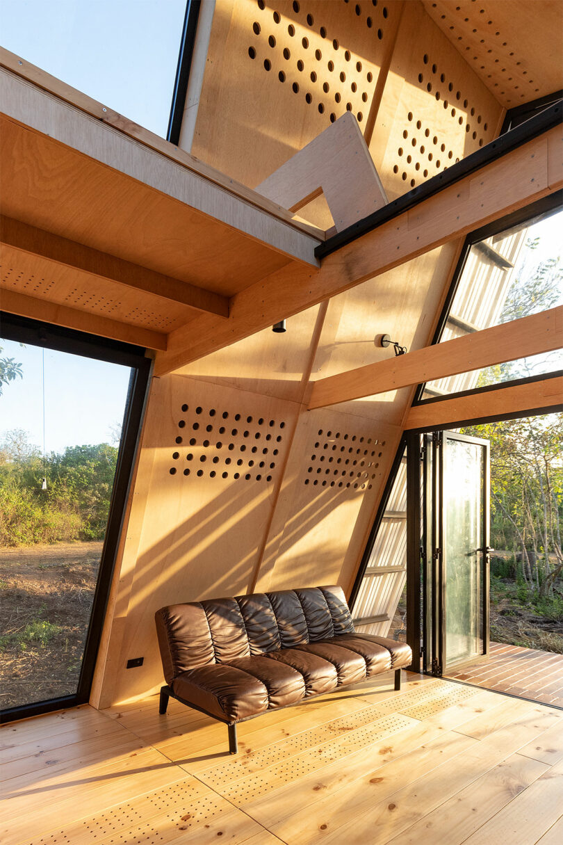 angled interior view of A-frame cabin with slanted wood walls and small brown sofa