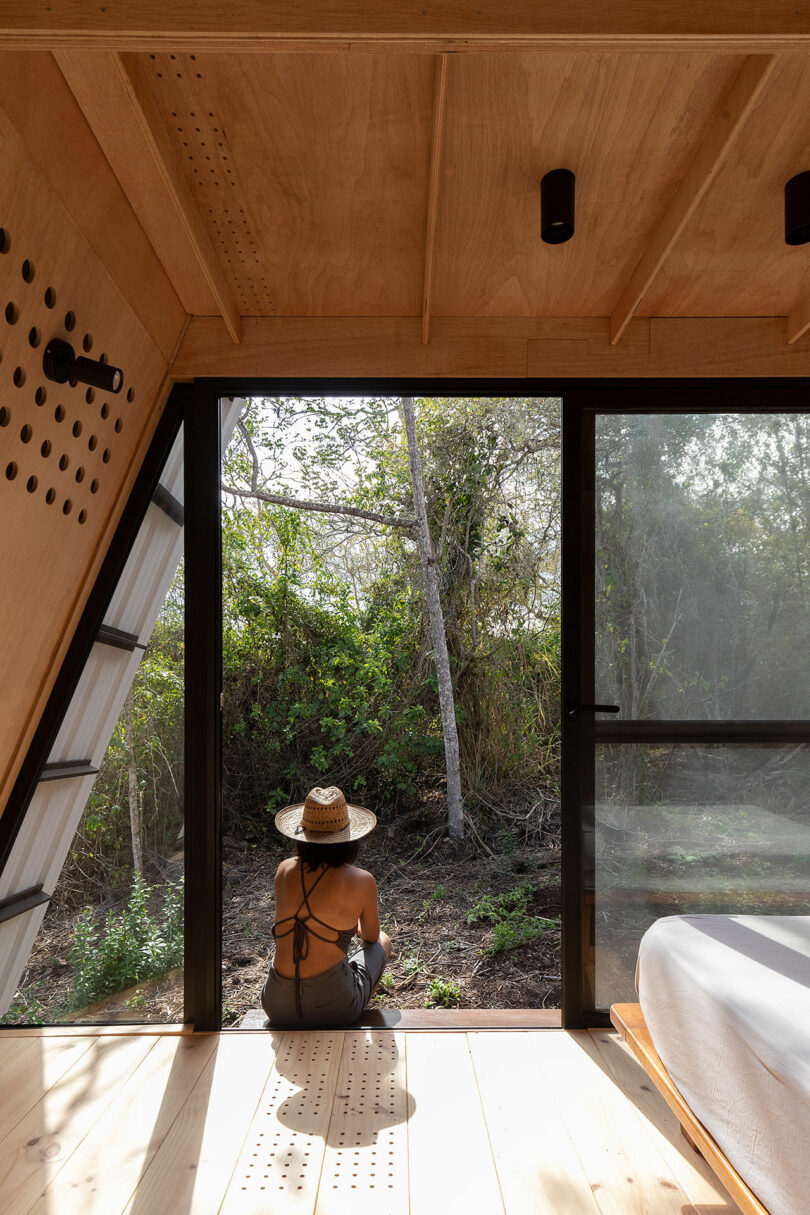partial interior view of minimalist cabin with woman sitting just outside on a porch